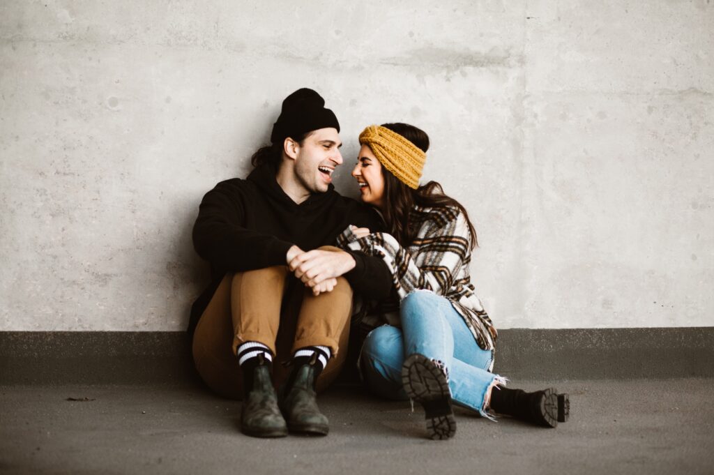 Young engaged couple laughing as they lean on urban parking garage wall in downtown St. Catharines.