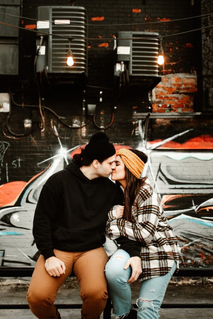Engaged couple kissing in urban downtown St. Catharines in front of graffiti wall.