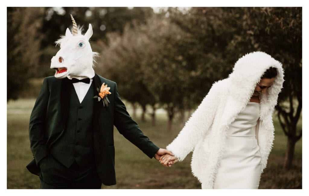 Married couple holding hands while groom sports unicorn mask at Kurtz Orchard, Niagara on the Lake.