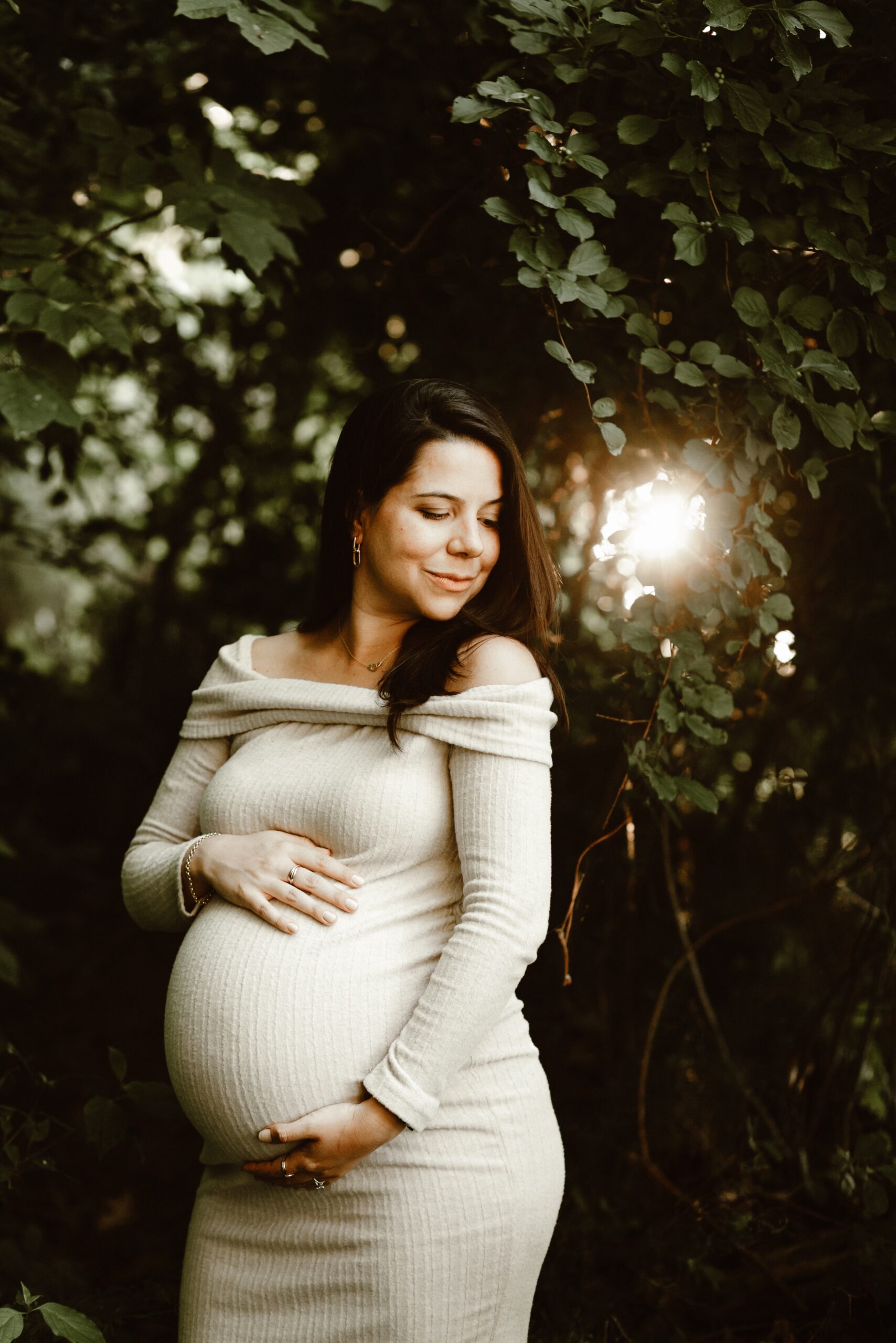 mother to be looking radiant in the woods as the sunlight comes through the trees