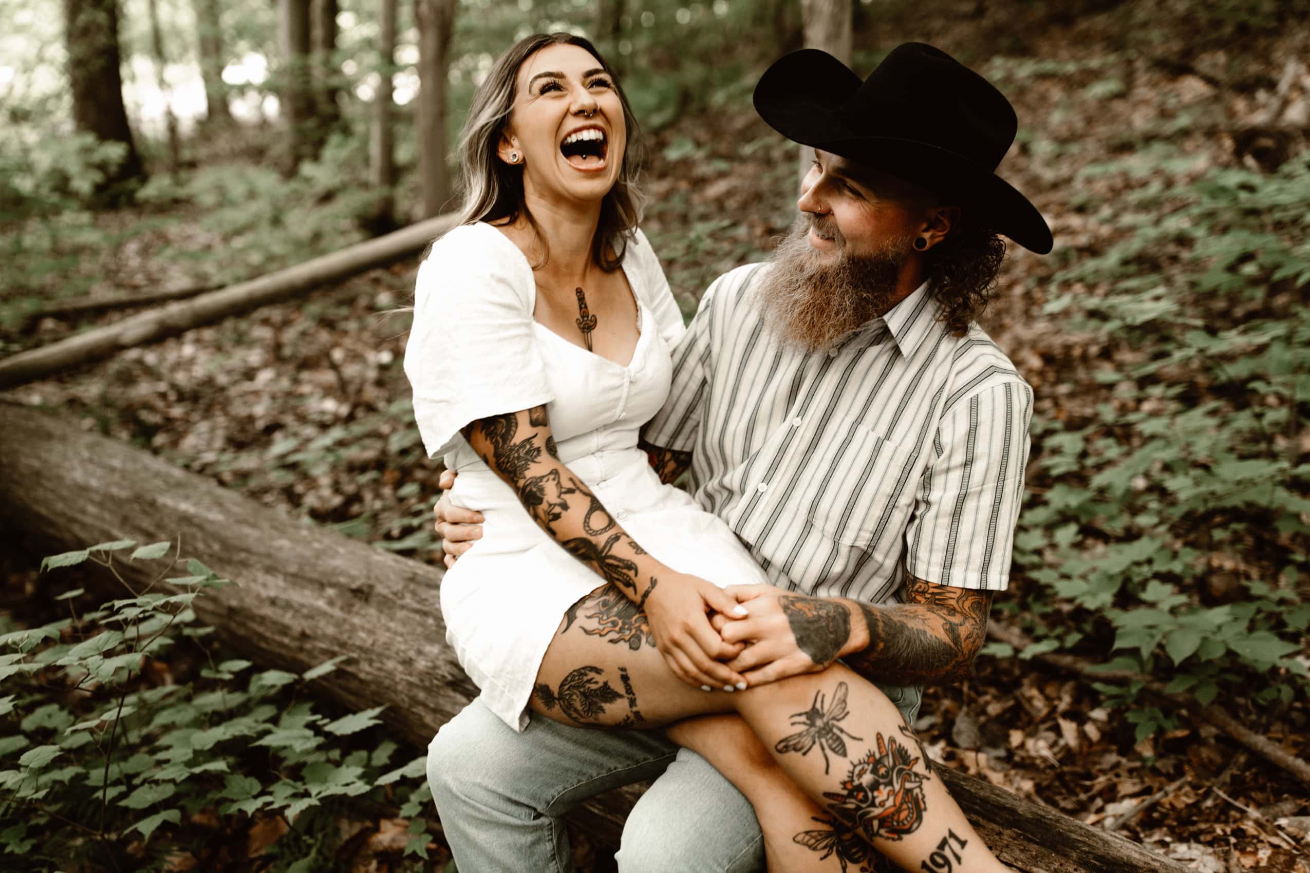 young couple sitting on a log in the woods laughing hysterically