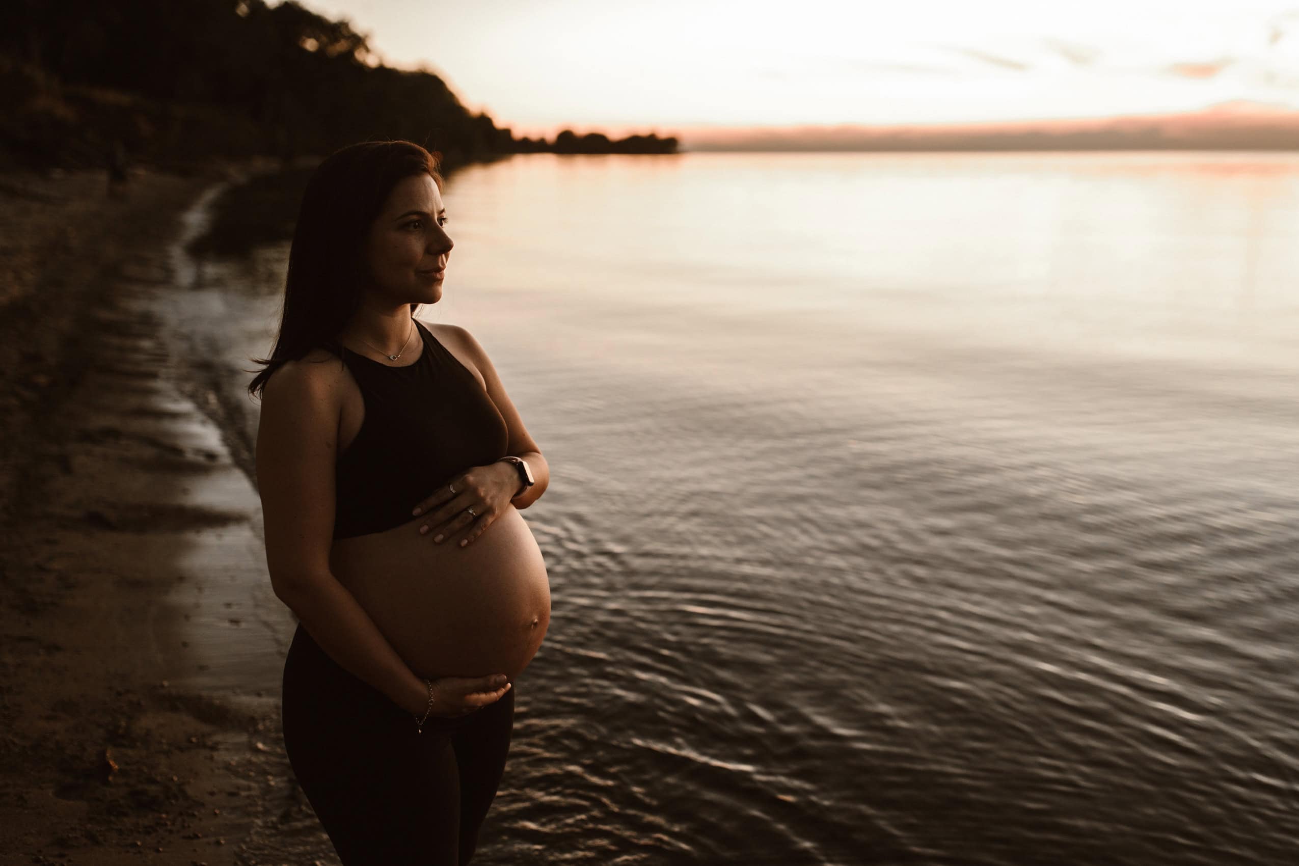 pregnant woman at the lake during sunset showing off her baby bump