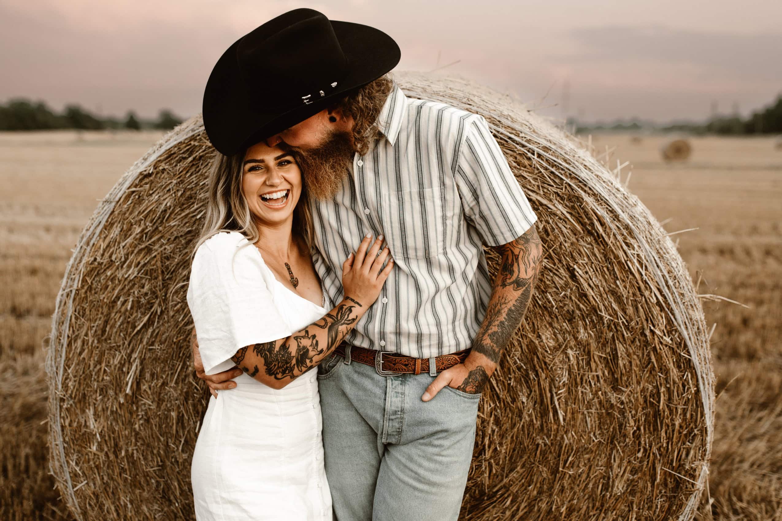 urban cowboy kissing his bride to be at sunset in a hay fienld