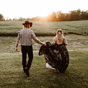 newly married niagara couple walking across field into the sunset 