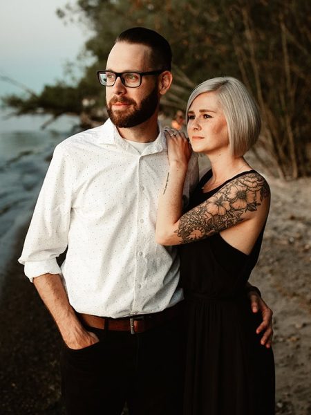 engaged couple looking into sunset on the shore of lake ontario